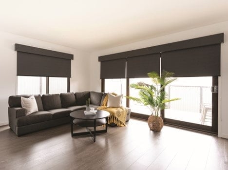 Blackout window blinds presented in a minimalistic room with a coach, table and a plant.