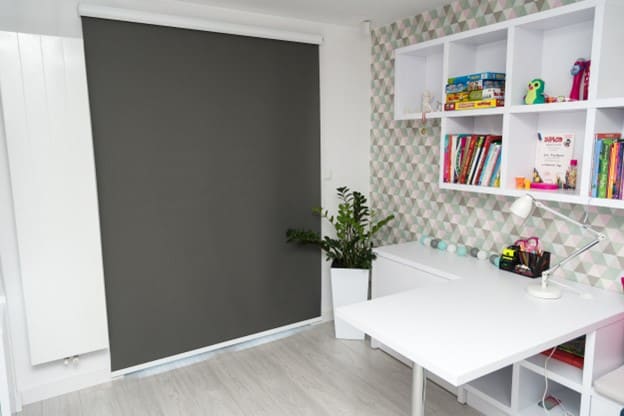 Blackout blind in a light decorated room with desk and shelving.