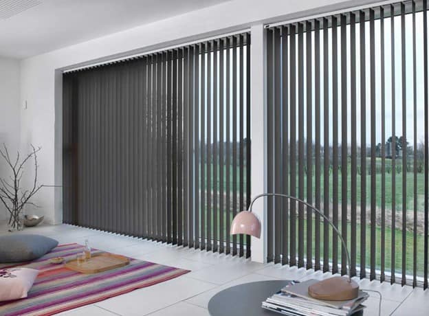 Vertical type blinds on a windows looking at a grass field.